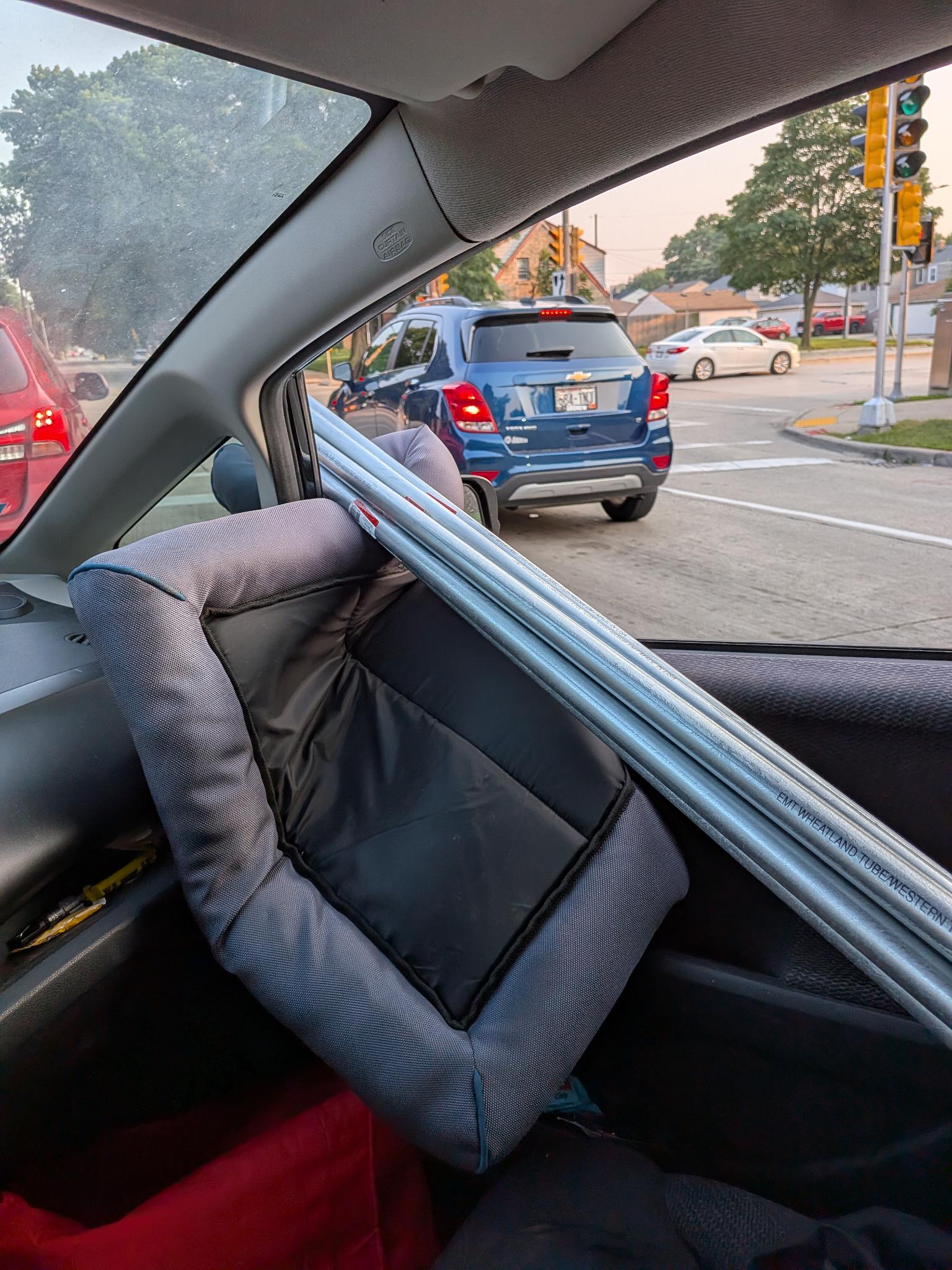 Ten-foot sticks of EMT conduit threaded through a Honda Fit at a stoplight
